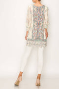 Long sleeve lace tunic top with embroidered hem, featuring a colorful printed back, styled with white leggings and beige heels.