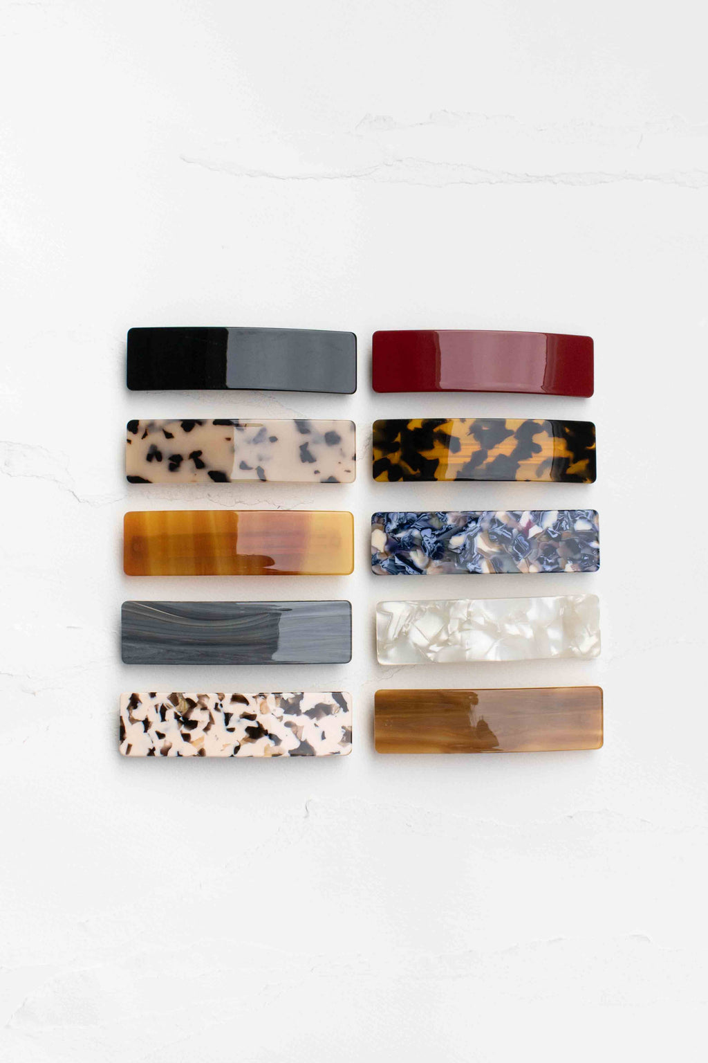 A collection of sleek rectangular hair barrettes in various colors and marbled patterns, showcasing a glossy finish.