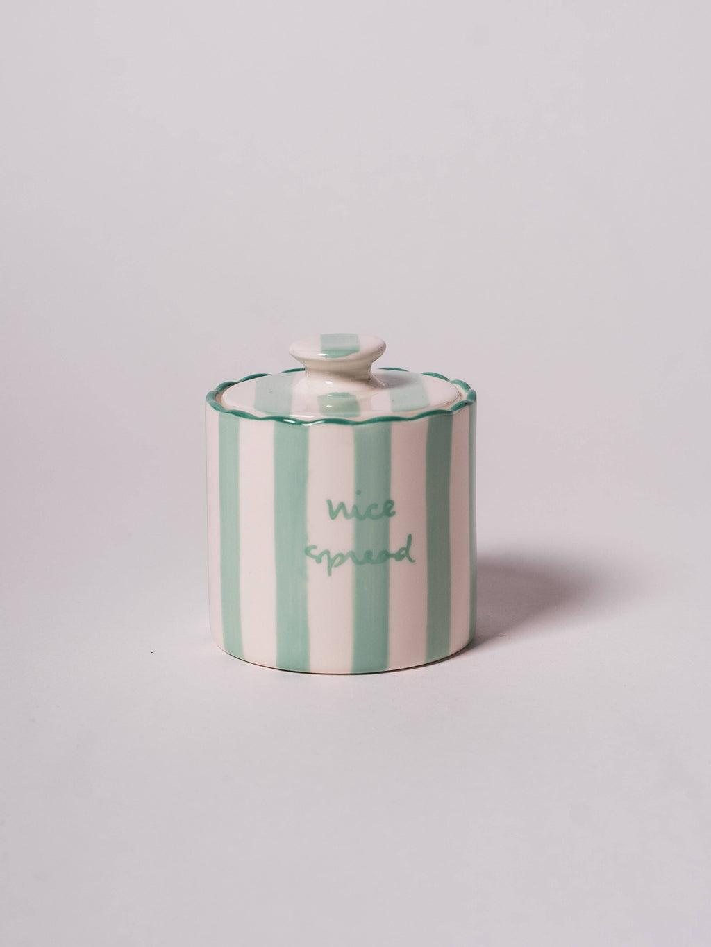 Round butter keeper with a lid featuring vertical green and white stripes and the phrase 'nice spread' on a scallop edge.