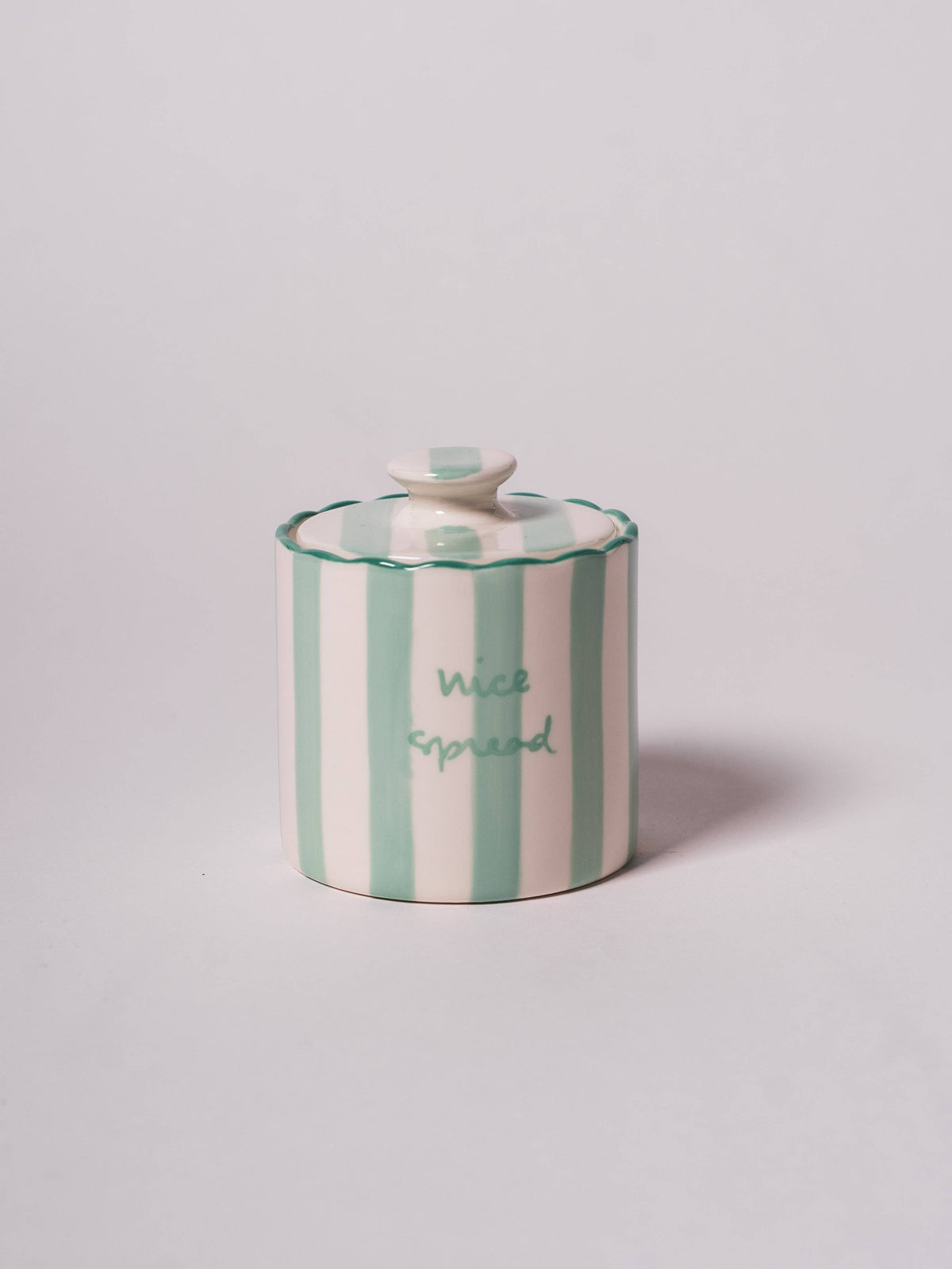 Round butter keeper with a lid featuring vertical green and white stripes and the phrase 'nice spread' on a scallop edge.