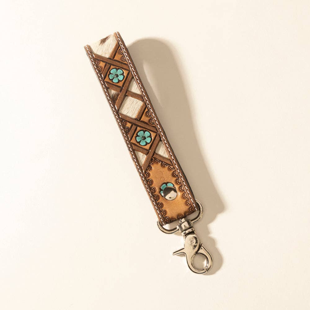 Handtooled leather keyfob featuring a natural hairon pattern in dark brown, white, and blue with decorative flowers and geometric shapes.