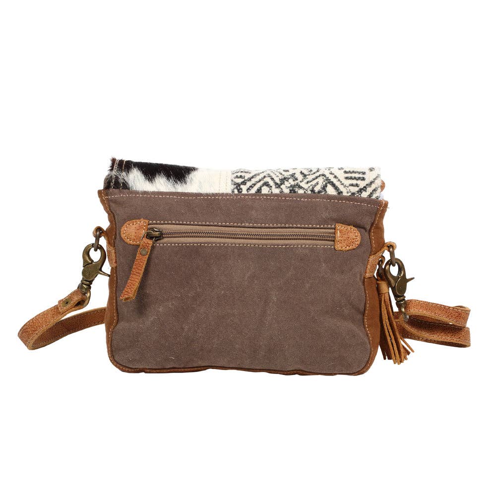 Geometric canvas messenger bag featuring a black-and-white hairon cowhide panel and tan leather accents.