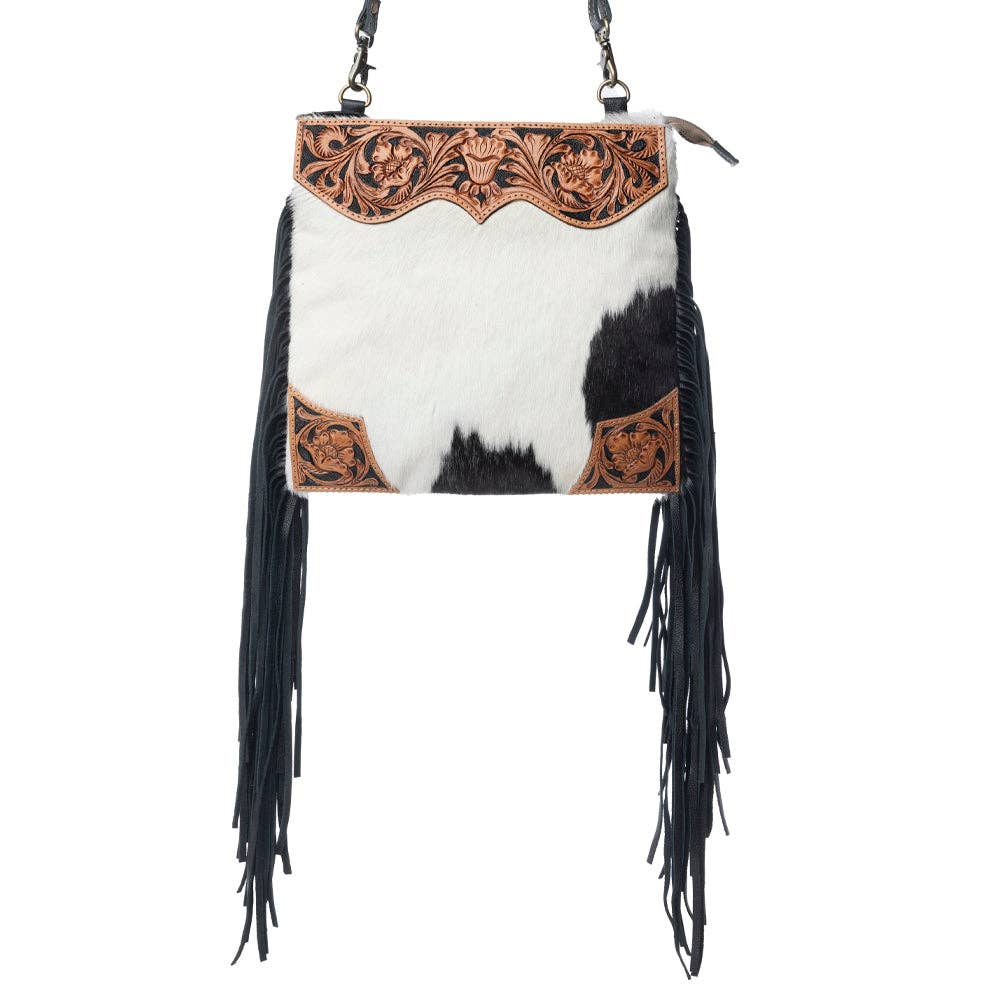 Hand-tooled caramel leather bag with hair-on hide front, scalloped top panel, and black leather fringe. Features zippered pockets and adjustable strap.