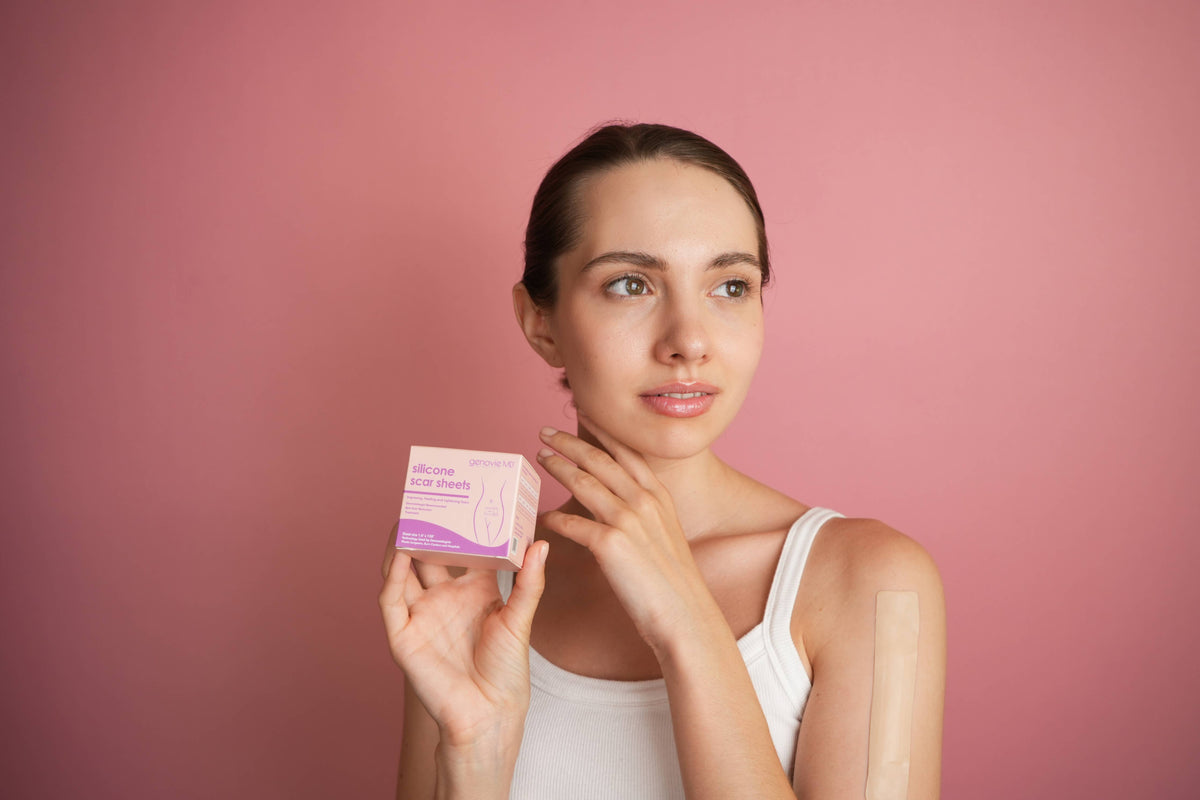 A person holding a pink box of scar treatment with a bandage on their arm.