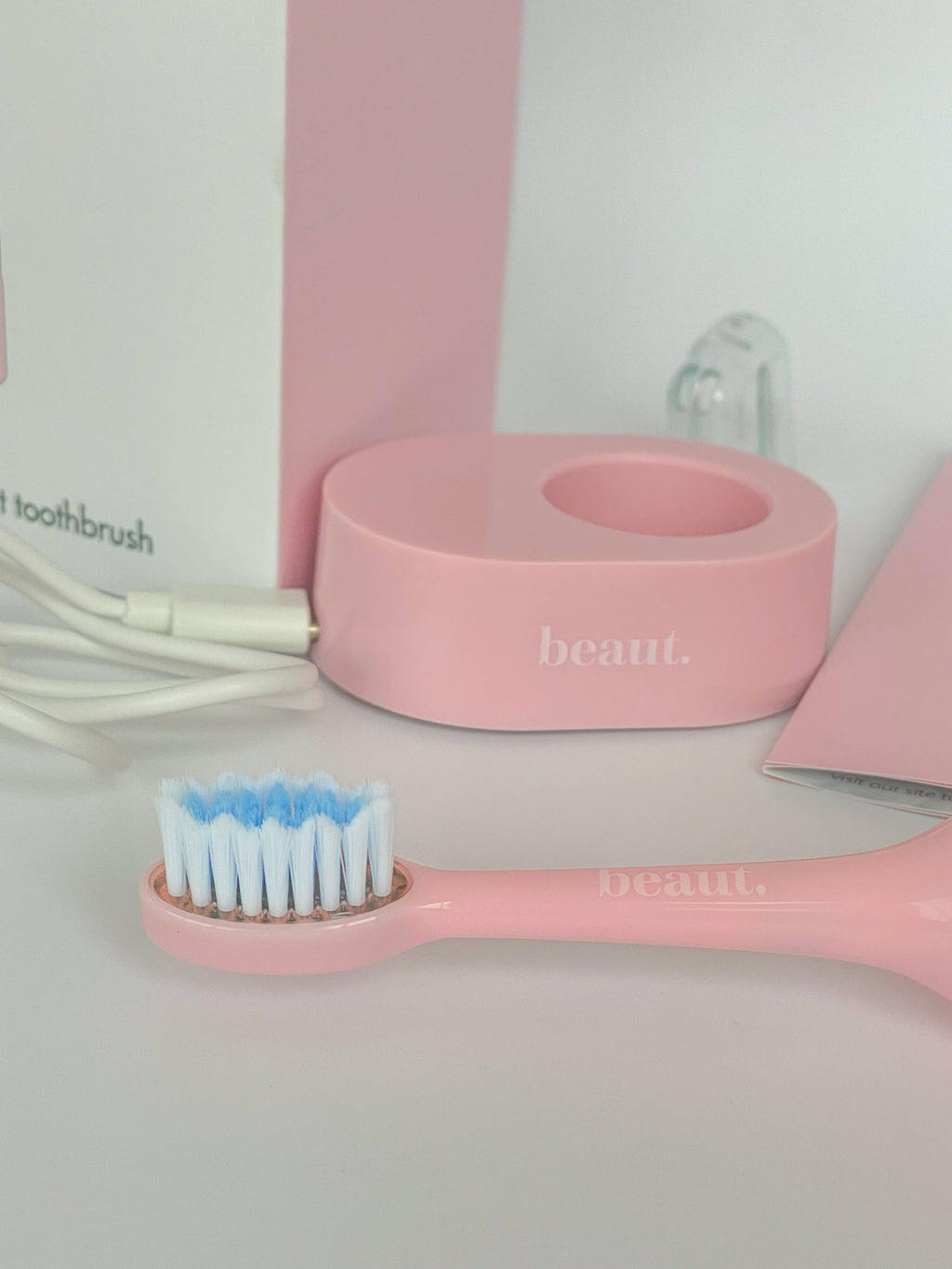 Pink Smile Kleen Sonic Vibration Toothbrush with white bristle head, charging base, and pink holder.
