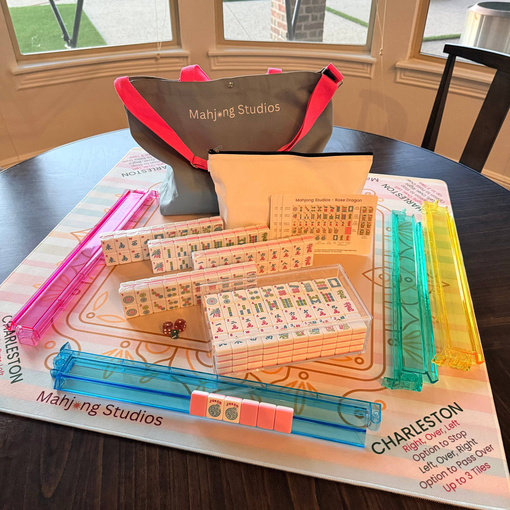 A vibrant Mahjong tile set featuring pink, blue, and clear plastic tiles, complete with a carrying bag and game mat.