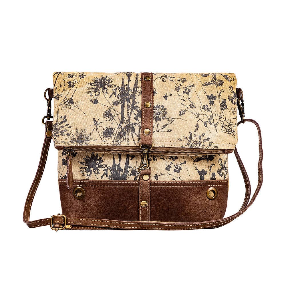 Floral canvas crossbody bag with chocolate leather bottom, fold-over flap, and adjustable shoulder strap.