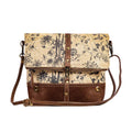 Floral canvas crossbody bag with chocolate leather bottom, fold-over flap, and adjustable shoulder strap.