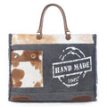 Handmade Print Weekender Bag featuring a mix of gray, brown, and cream colors with leather handles and a decorative front pocket.