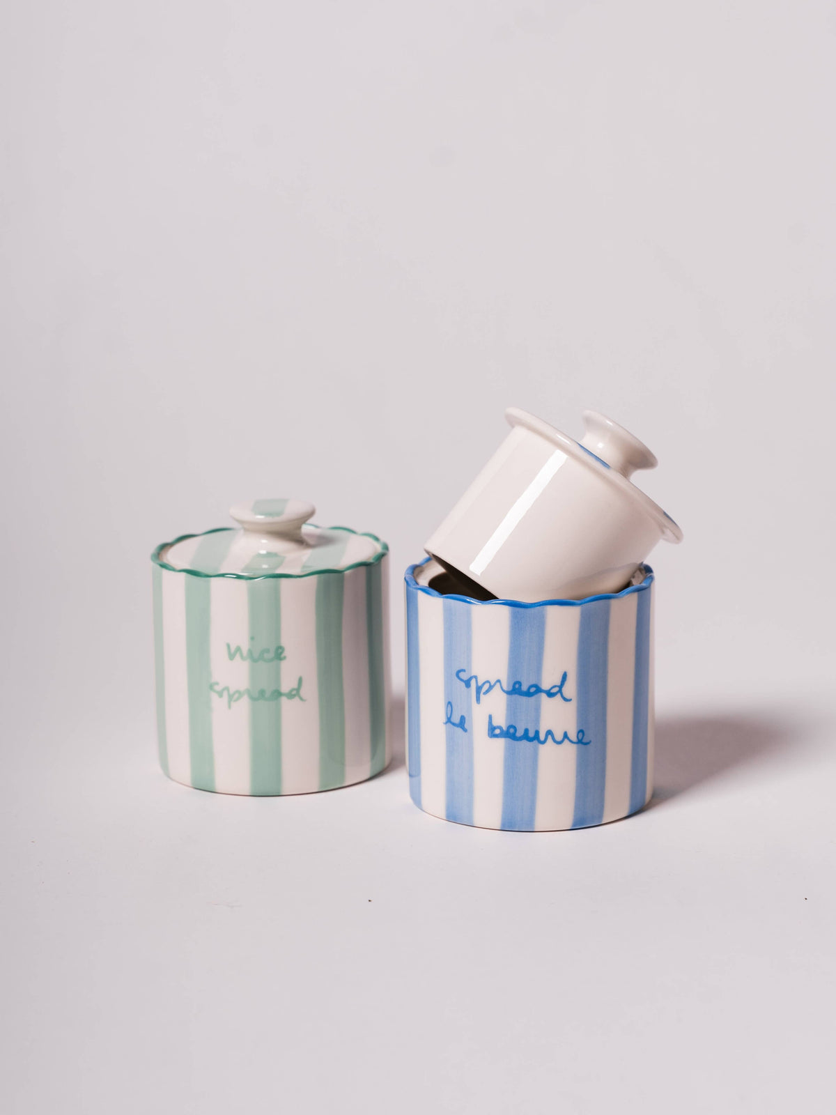 Two Kinsey Scallop Butter Keepers with playful designs, one green with 'nice spread' and one white with 'spread le beurre.'