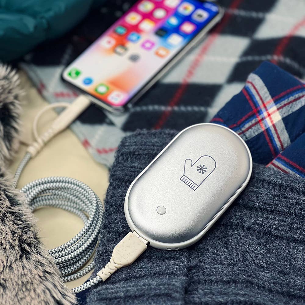 Hand warmer with a rounded design, button, and snowflake symbol, alongside a smartphone and charging cable.