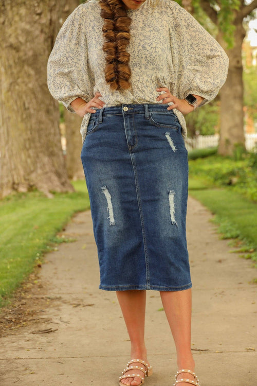 Knee-length denim skirt featuring a fitted silhouette, front and back pockets, and stylish distressing on the front.
