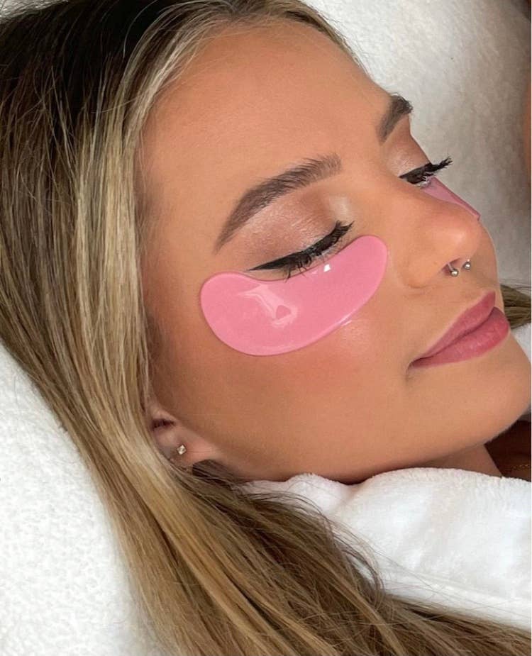 Person applying hydrating pink under-eye masks for a refreshing treatment. Eye Luv masks help depuff and brighten the under-eye area.