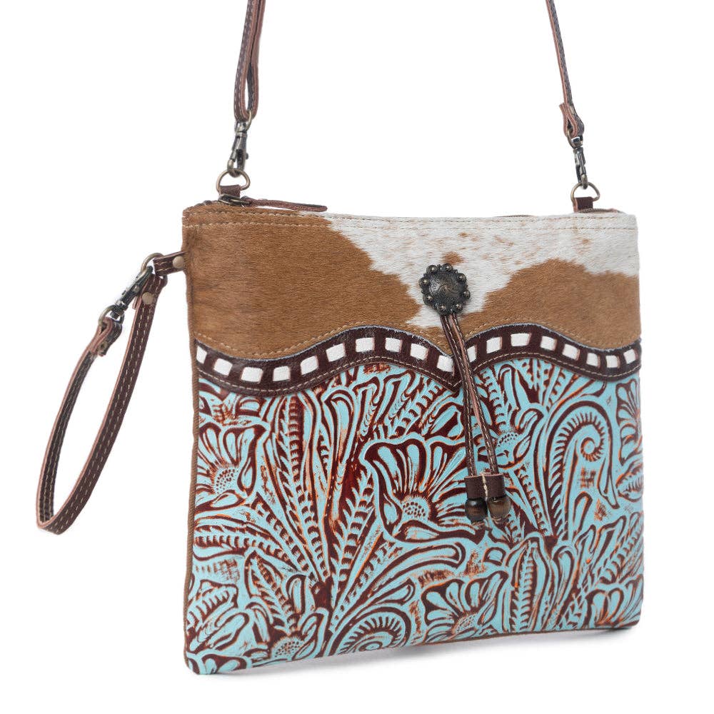 Turquoise embossed leather crossbody bag with brown-and-white cowhide accents and floral patterns.