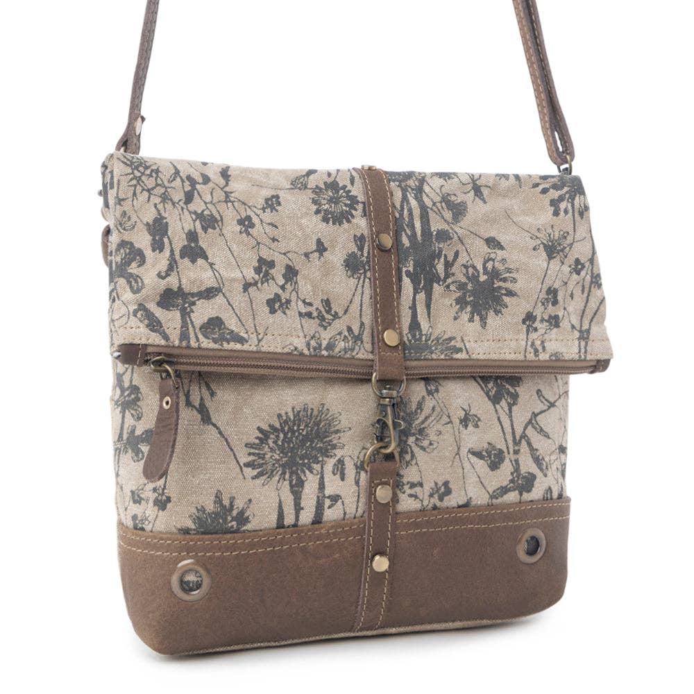 Floral canvas crossbody bag with chocolate leather bottom, fold-over flap, zipper closure, and adjustable strap.