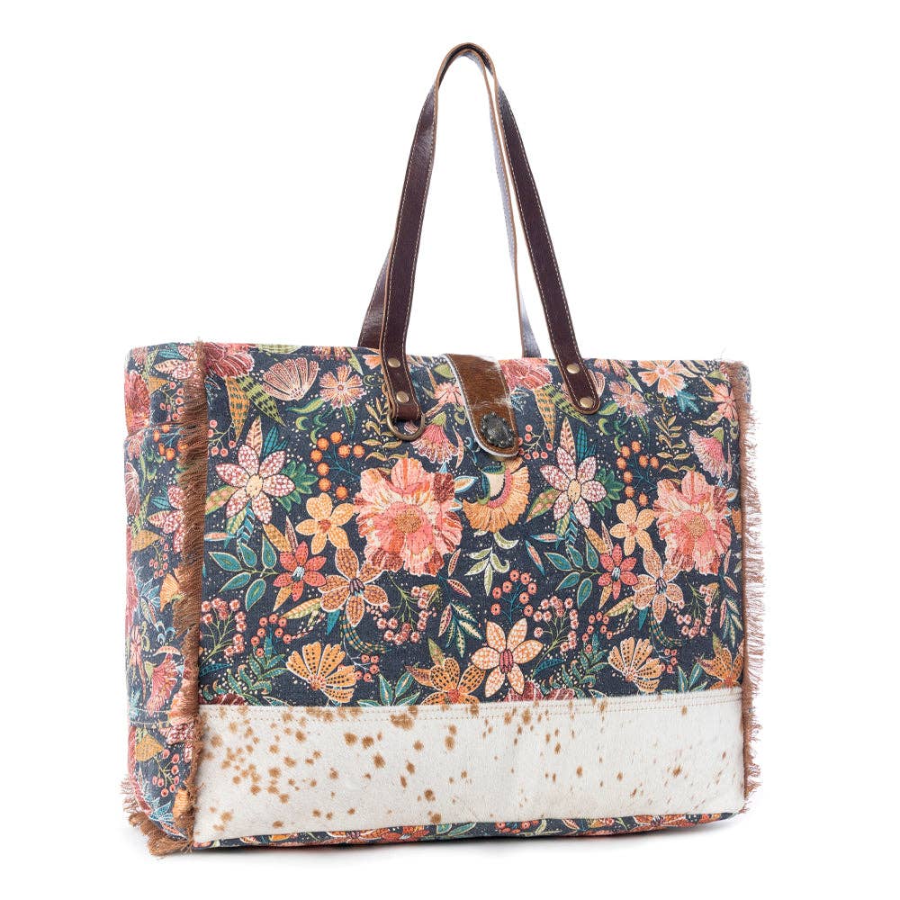 Floral-patterned Fyole Weekender Bag with leather handles and fringe detail, featuring a hairon section at the bottom.