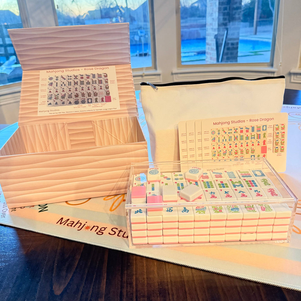 Mahjong tile set arranged in a clear container, featuring vibrant designs and a white pouch for storage.