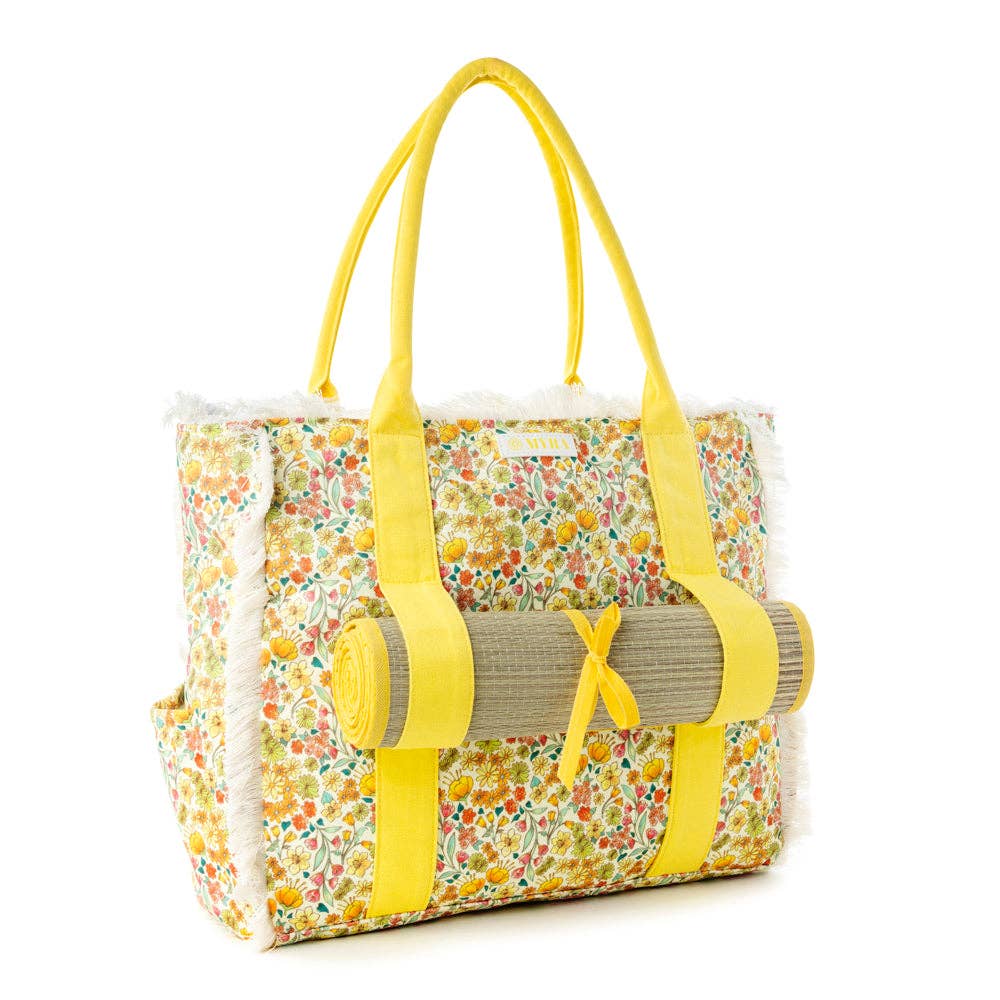 Wildflower print weekender bag with fringe detailing, yellow carry straps, and a rolled beach mat secured with a bow.