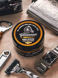 Round container of The Gentleman Hand Rescue with a Citrus & Mahogany scent, featuring a black lid and labeled 'Hand Rescue'.