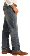 Dark vintage jeans with a stackable design draping over brown cowboy boots, featuring visible stitching and back pockets.